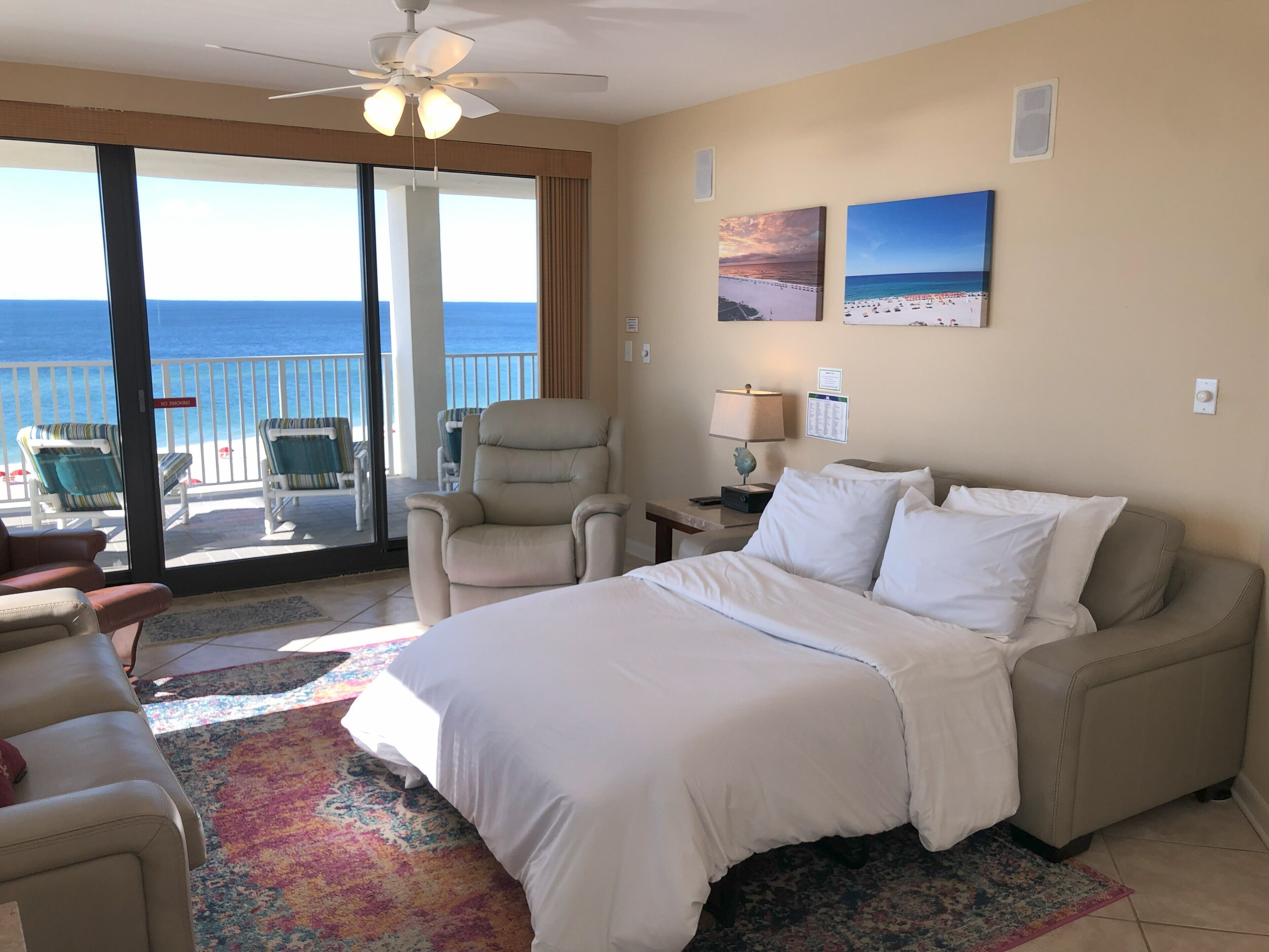A hotel room with a bed, a chair, a desk, a lamp, and a view of the ocean through a sliding door.