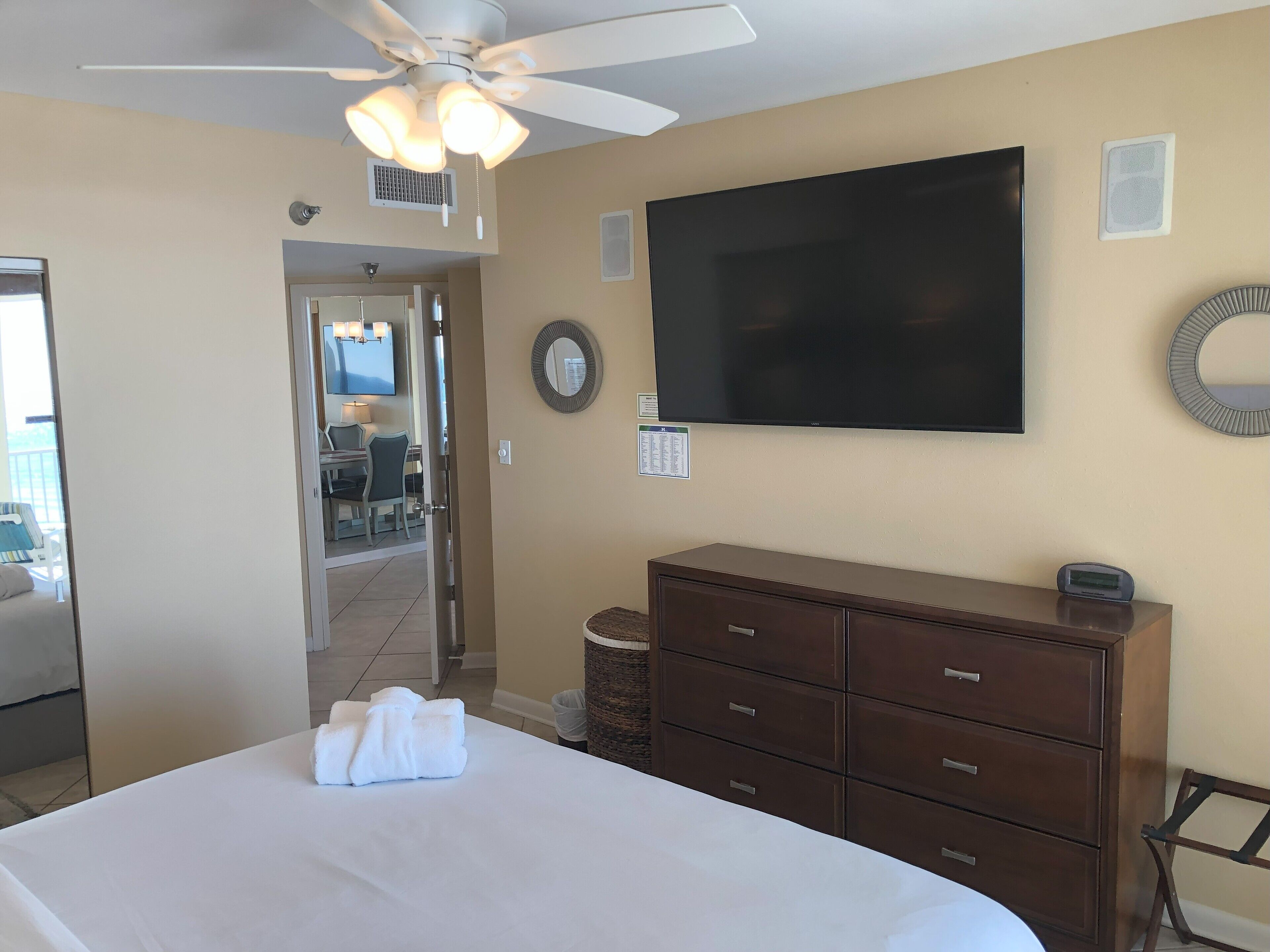 A hotel room with a bed, a dresser, a ceiling fan, a TV, and a view of the dining area.