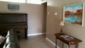 A living room with a piano, a couch, a small table with books, a lamp, and a painting on the wall. -  Sleeps 12 ; within walking distance to shops; boat parking 9ft x 30ft  NO tower (Page)