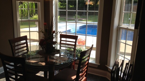 A dining area with a glass table and chairs, a vase with flowers, and a view of a swimming pool through large windows.