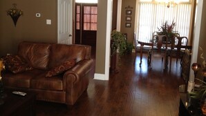A living room with a brown leather sofa, a dining area with a wooden table and chairs, and a hallway leading to another room.
