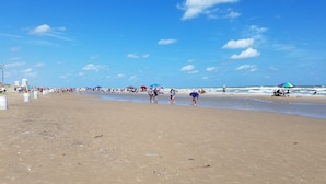 A wide sandy beach with people walking and sitting under umbrellas.