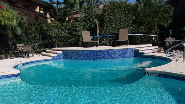 A clear blue pool with a 5 ft depth marker, surrounded by lounge chairs and a tiled deck.