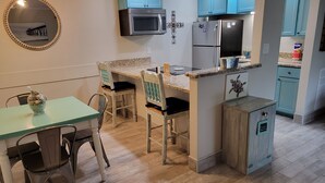 A compact kitchen with teal cabinets, a microwave, a refrigerator, and a dining area with a table and chairs.
