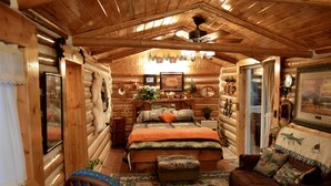 A log cabin interior with a wooden ceiling, a bed with an orange blanket, a wooden bench, and a brown sofa with decorative pillows. - Relaxing, spacious cabin w/ hot tub and Starlink's high-speed internet service (Darby)