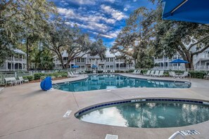 A pool area with lounge chairs and umbrellas, surrounded by trees and a building with balconies. - FREE GOLF, TENNIS, POOLS & BEACH MANAGED BY WESTIN RESORT & SPA- 3 Bdrm/3 BATH  (Hilton Head Island)