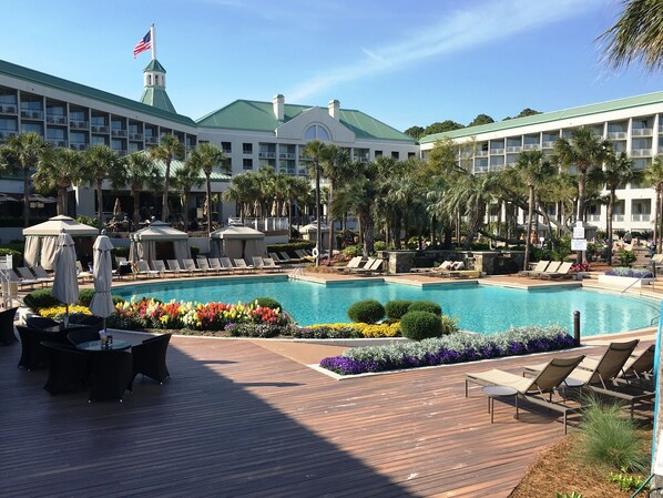 A resort pool area with lounge chairs, umbrellas, and a flag on a building in the background. - FREE GOLF, TENNIS, POOLS & BEACH MANAGED BY WESTIN RESORT & SPA- 3 Bdrm/3 BATH  (Hilton Head Island)