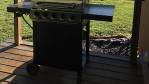 En transportabel grill på en træterrasse med en græsplæne og træer i baggrunden.