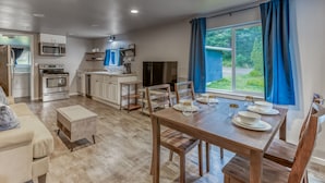 Una cocina moderna con electrodomésticos integrados, un comedor con una mesa y sillas de madera, y un amplio ventanal con cortinas.