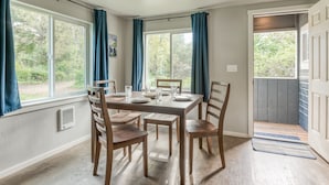 Comedor con una mesa lista para cuatro, sillas de madera y ventanas amplias con cortinas.