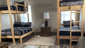 Een kamer met twee stapelbedden, een klein houten nachtkastje met een lamp en een ventilator.