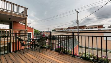 Une terrasse en bois avec deux chaises et une table, donnant sur un quartier résidentiel avec des maisons et un immeuble à la façade rouge.