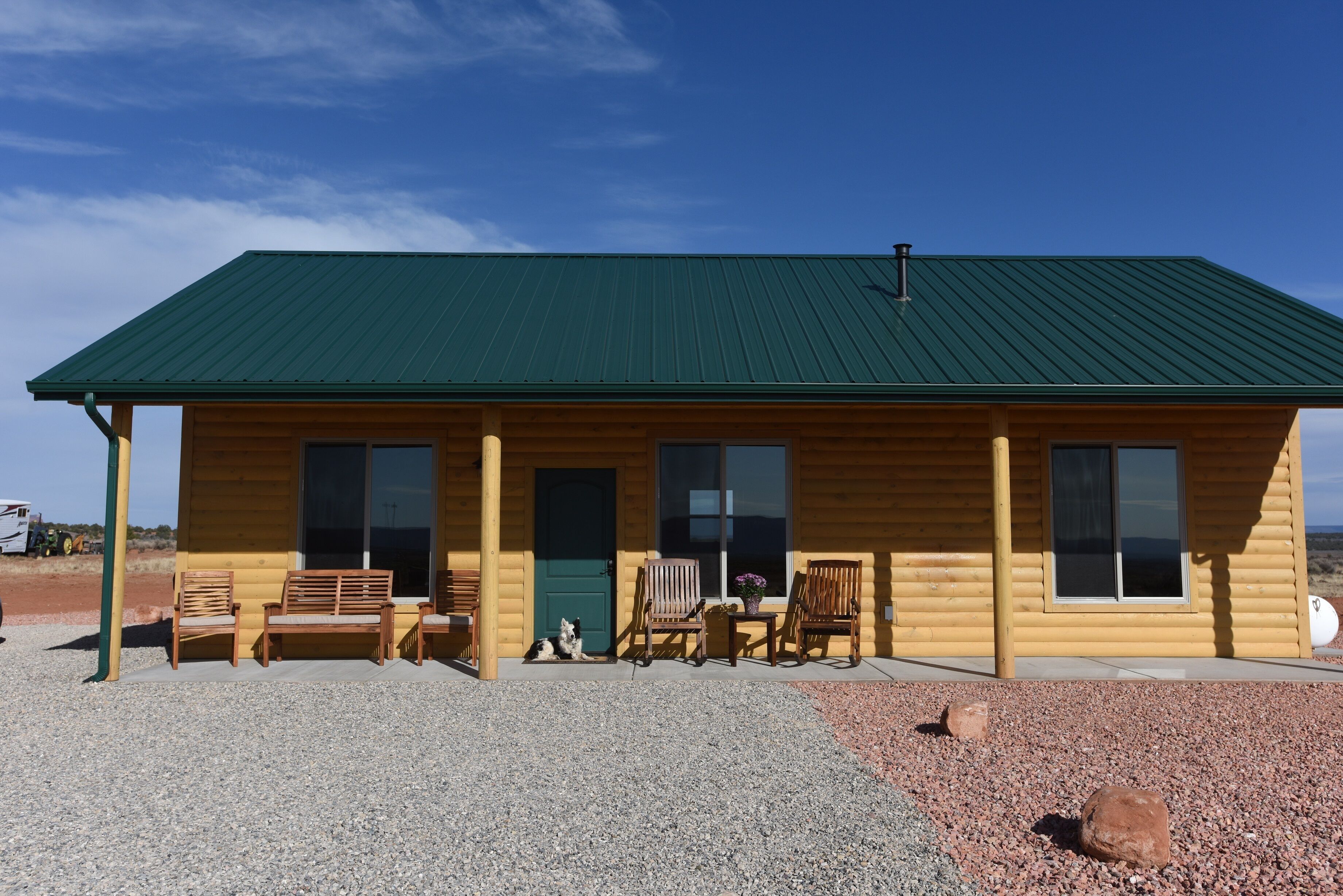 A log cabin with a green metal roof, wooden exterior, and a gravel driveway.