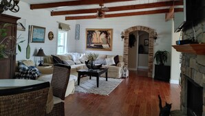 A cozy living room with wooden beams, a fireplace, a sofa, a coffee table, and a painting of a sailboat.