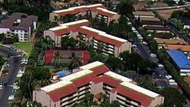 Luchtbeeld van een resort met meerdere gebouwen, een tennisbaan en uitzicht op de oceaan.