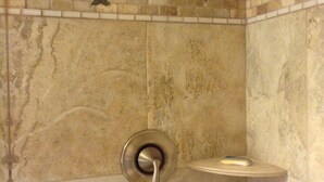 Een douche met een marmeren wand, een tegeltapijt met dolfijnen en een zeepbakje.