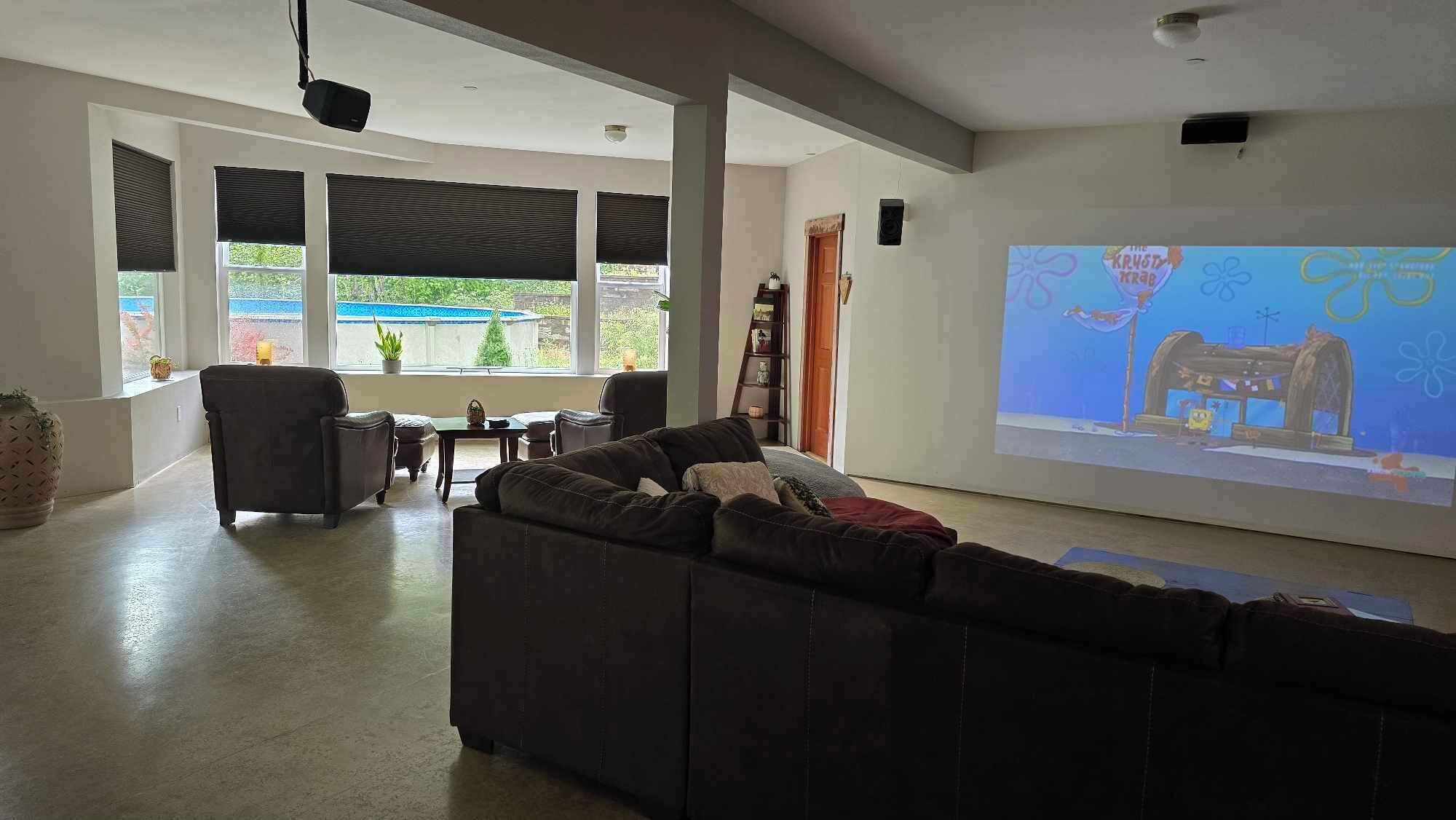 Een ruime woonkamer met een grote bank, een salontafel en een televisiescherm waarop een tekenfilm wordt vertoond.
