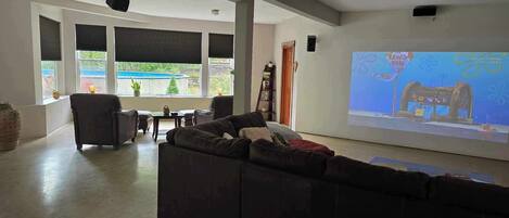 Een ruime woonkamer met een grote bank, een salontafel en een televisiescherm waarop een tekenfilm wordt vertoond.
