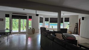 Ein geräumiges Wohnzimmer mit einer großen Couch, einem Esstisch und mehreren Fenstern, die Blick auf Grünflächen bieten.