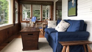 Een gezellige kamer met een blauwe bank, een houten kist en een rieten stoel.