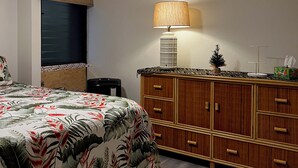 A bedroom with a bed, a wooden dresser, a ceiling fan, and a window with blinds. - UPDATED MAUI VACATION RENTAL (Kihei)