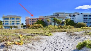 A beachfront property with multiple buildings, including a yellow building with balconies and a pink building with a red roof. - Beautifully Updated Madeira Bay Resort Unit 401 - Steps from Sand and Fun! (Madeira Beach)
