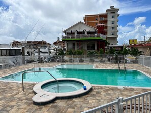 Una piscina con hidromasaje, rodeada por un solárium con baldosas y una valla blanca.