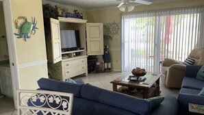 A living room with a sofa, a coffee table, a television on a stand, and a ceiling fan.