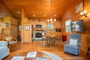 L’intérieur d’un chalet en bois comprend un coin repas, une cuisine et une grande fenêtre donnant sur une cascade.