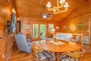 L’intérieur d’un chalet en bois comprend une table à manger, des chaises, un canapé, un ventilateur de plafond et des lampes fixées au mur.