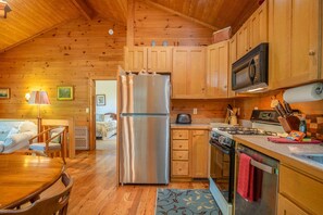 L’intérieur d’un chalet en bois comprend une cuisine, un coin repas et une chambre à coucher visible.
