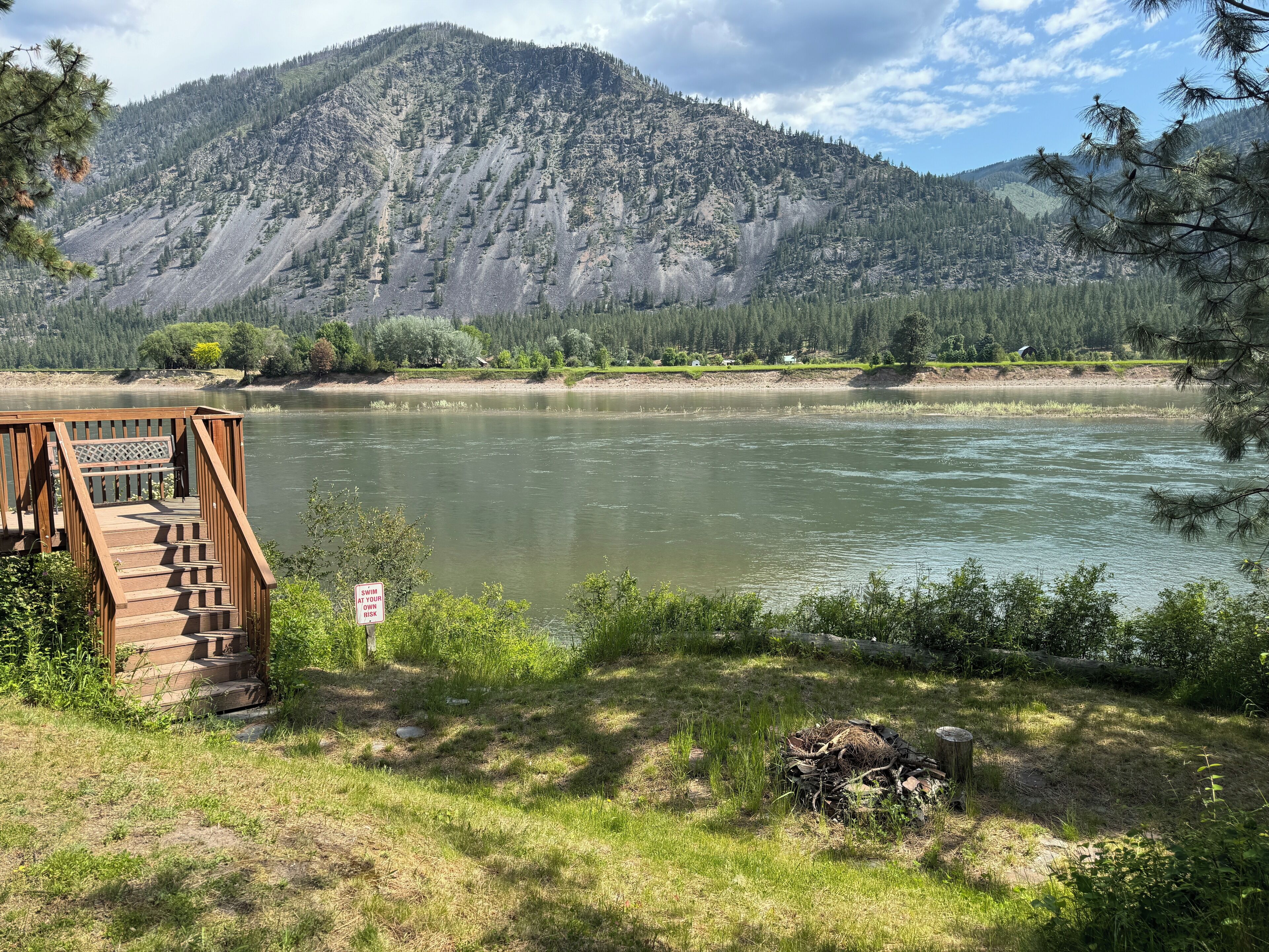 A wooden deck overlooking a river with a mountain backdrop.