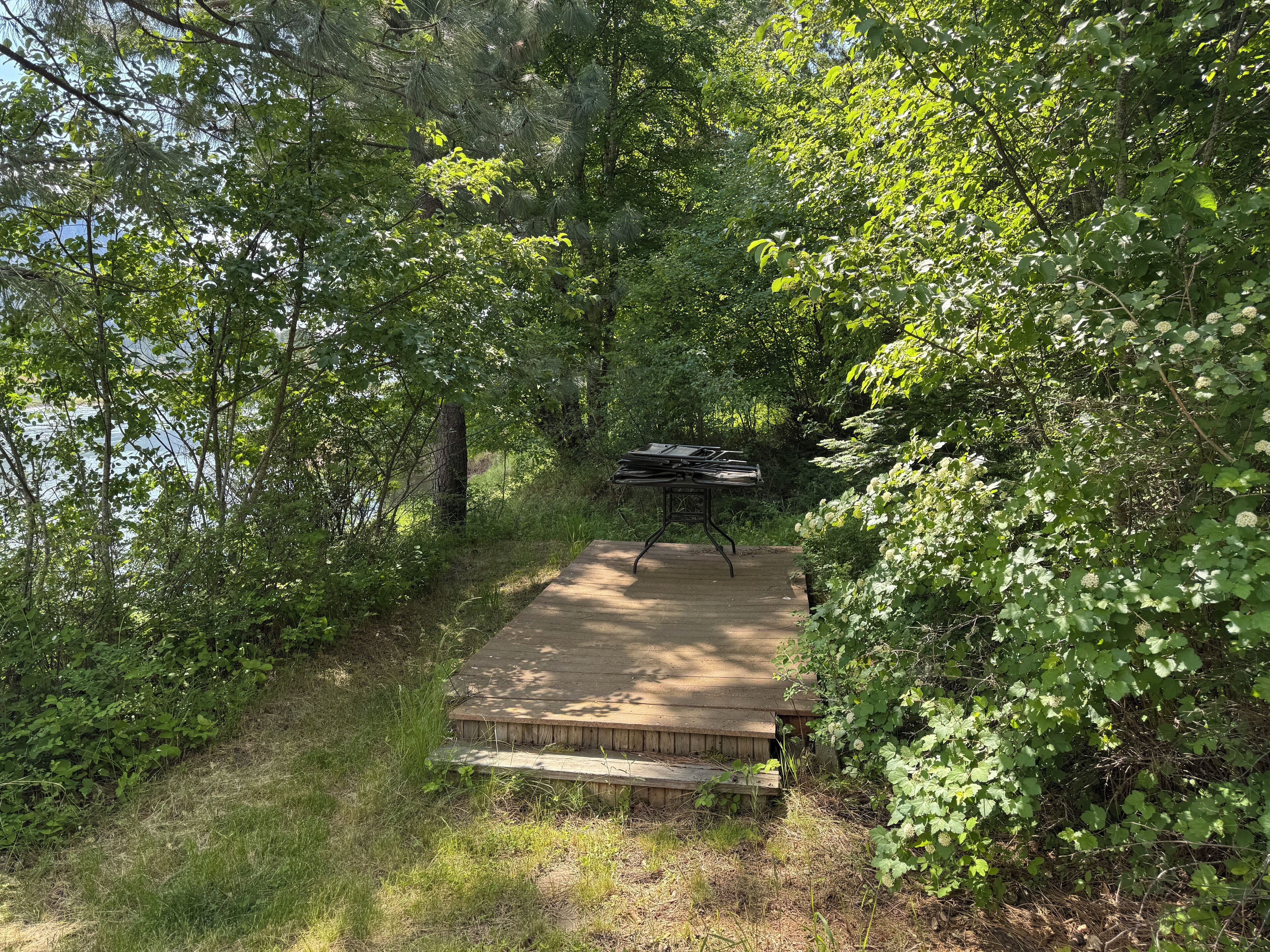 A wooden deck with a grill in a forested area.