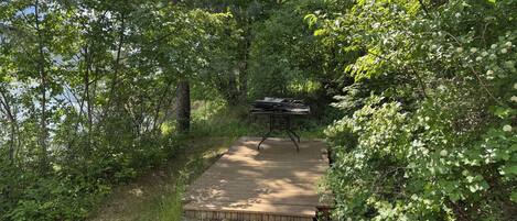 A wooden deck with a grill in a forested area.