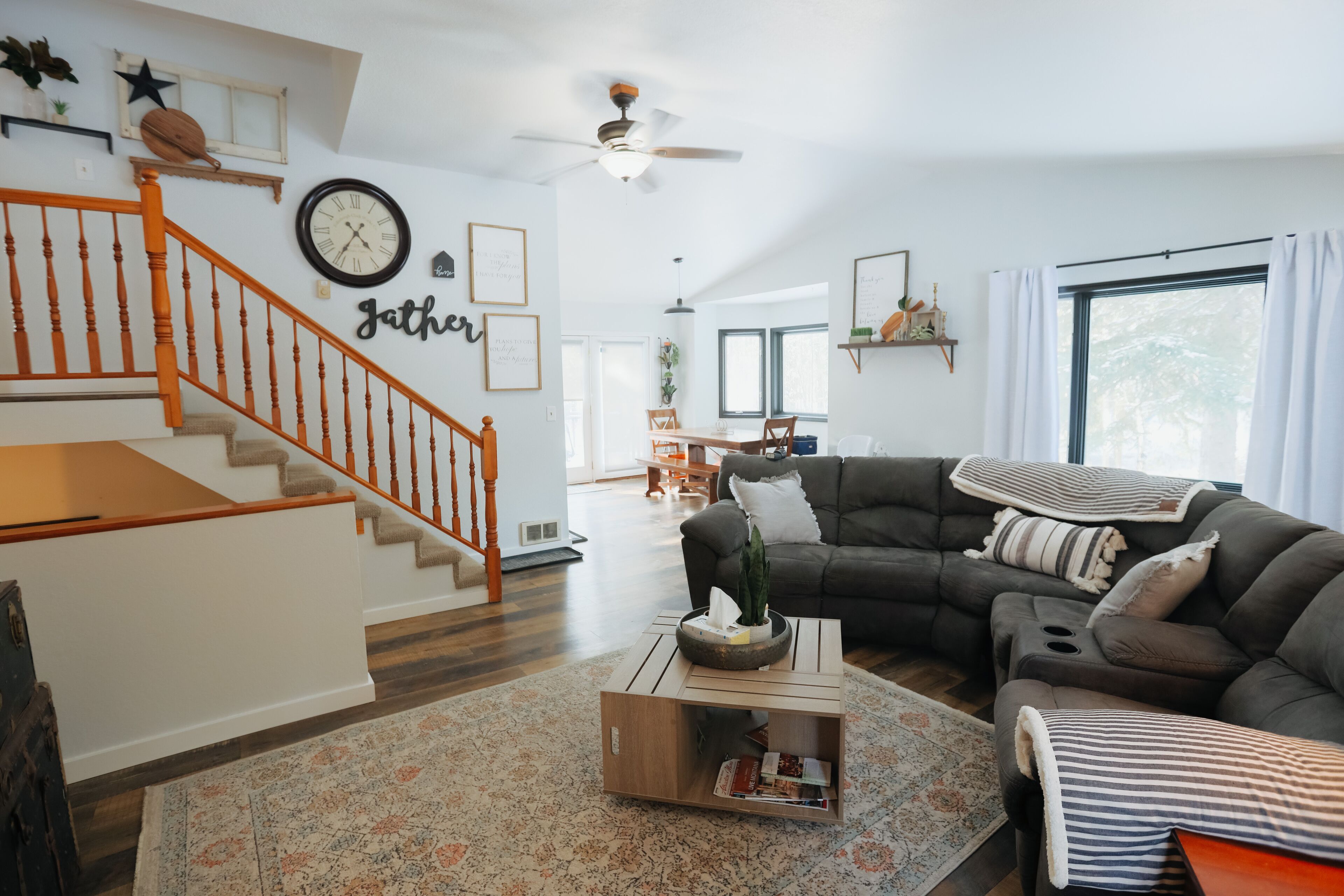 A spacious living room with a staircase, a large window, and a ceiling fan.