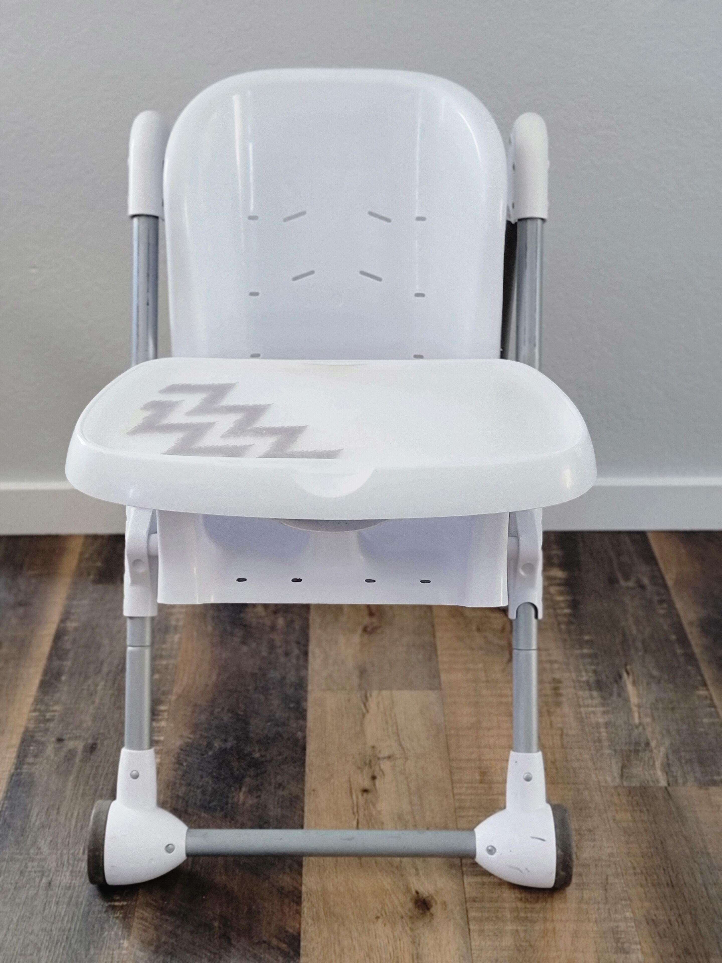 Un déambulateur blanc doté d’un siège et d’un dossier rembourrés, et dont l’assise présente un motif en zigzag.