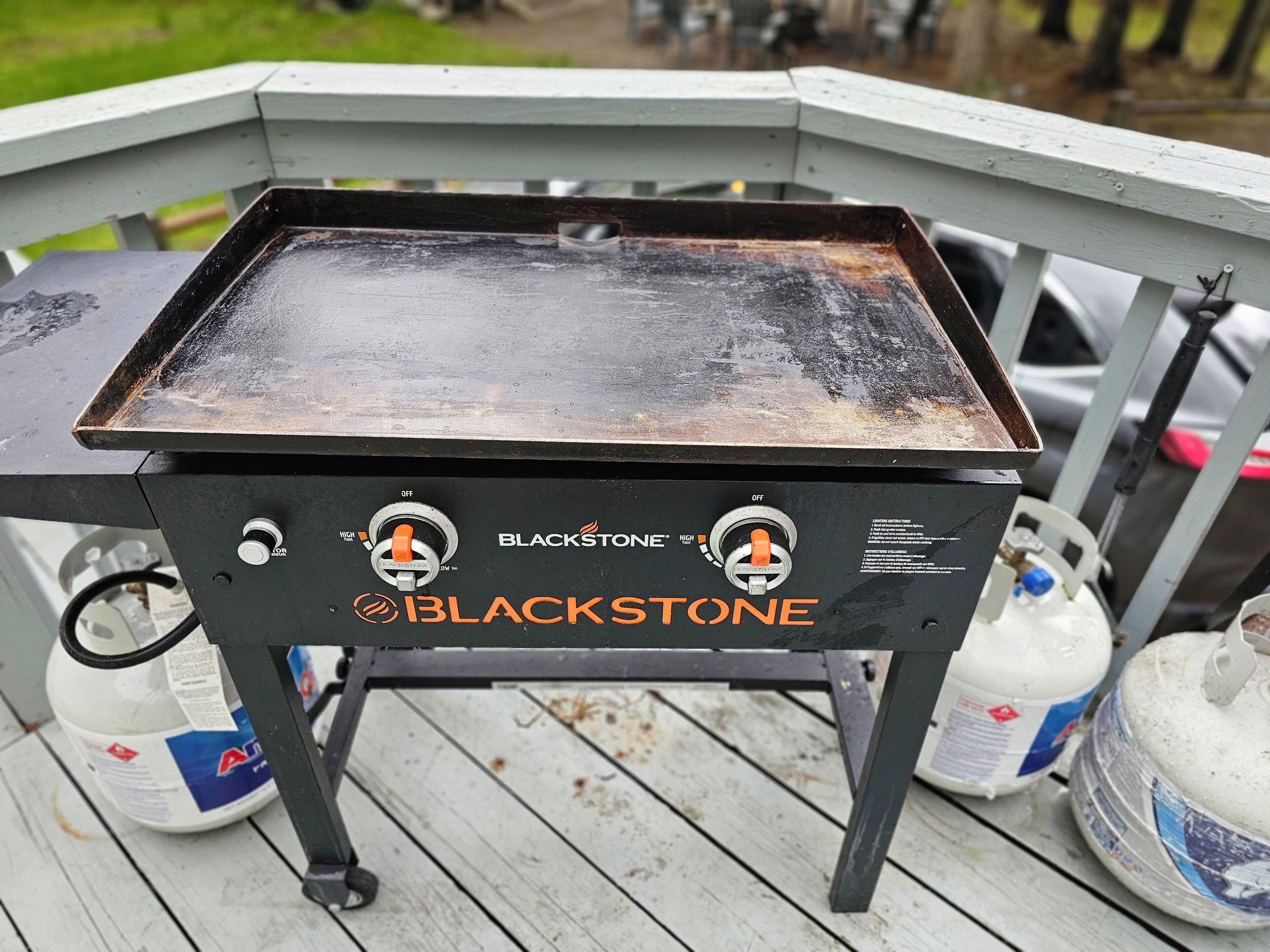 A Blackstone grill on a wooden deck with propane tanks nearby.