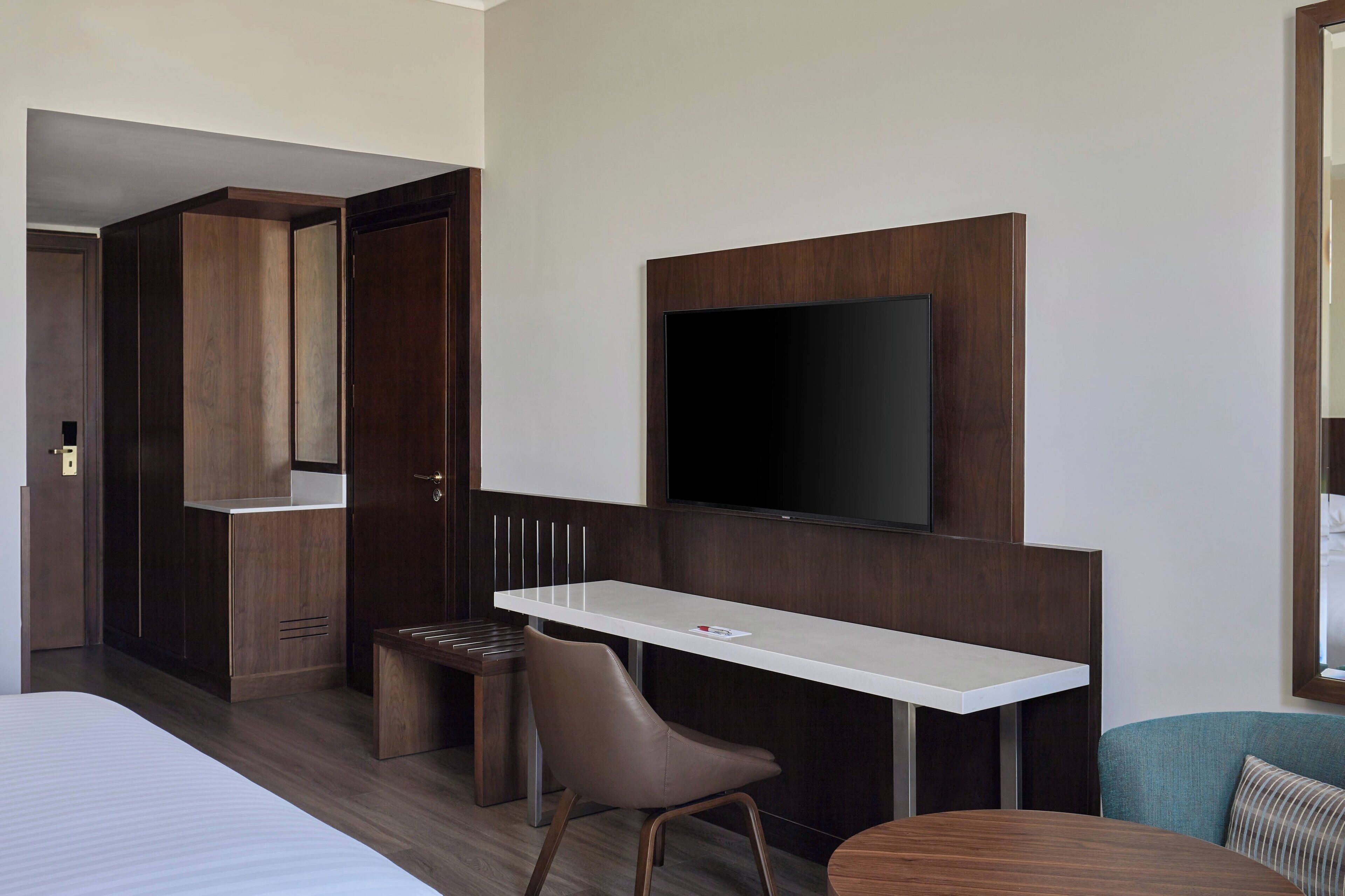 Ein Hotelzimmer mit Bett, Schreibtisch mit Stuhl, Wandfernseher und einem kleinen Tisch.