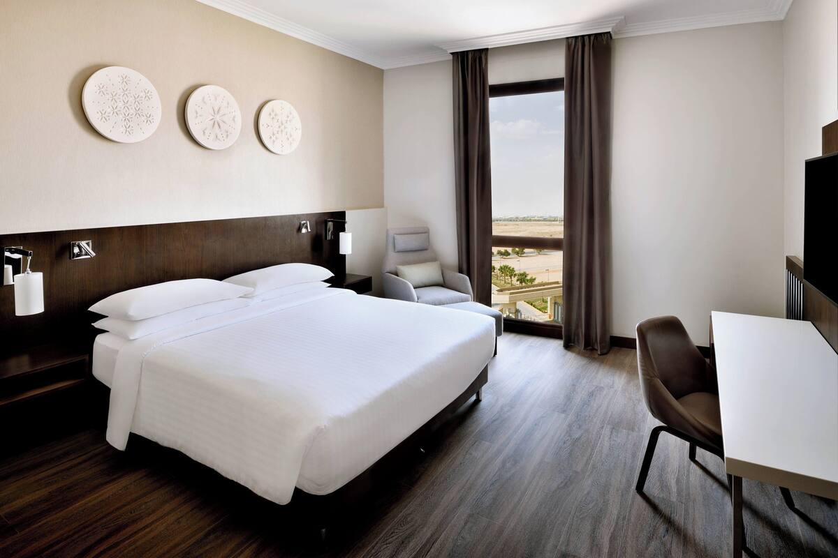 Ein Hotelzimmer mit einem großen Bett, einem Schreibtisch, einem Stuhl und Blick ins Freie.