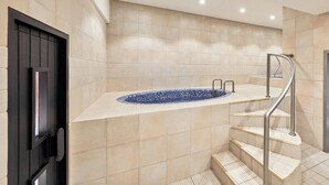 Un baño moderno con una bañera independiente, una puerta negra y una escalera con barandillas metálicas.