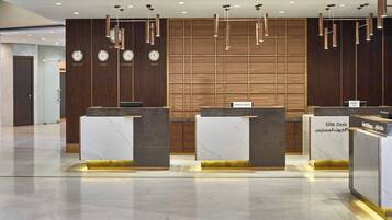 A hotel reception area with marble counters, wooden paneling, and clocks indicating different time zones.