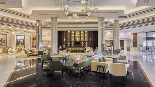 Un lobby amplio con una zona de estar central, un mostrador de recepción y un candelabro moderno.
