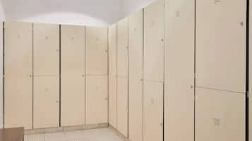 A row of beige lockers numbered 1 to 15, with a tiled floor and a wooden bench in the foreground.