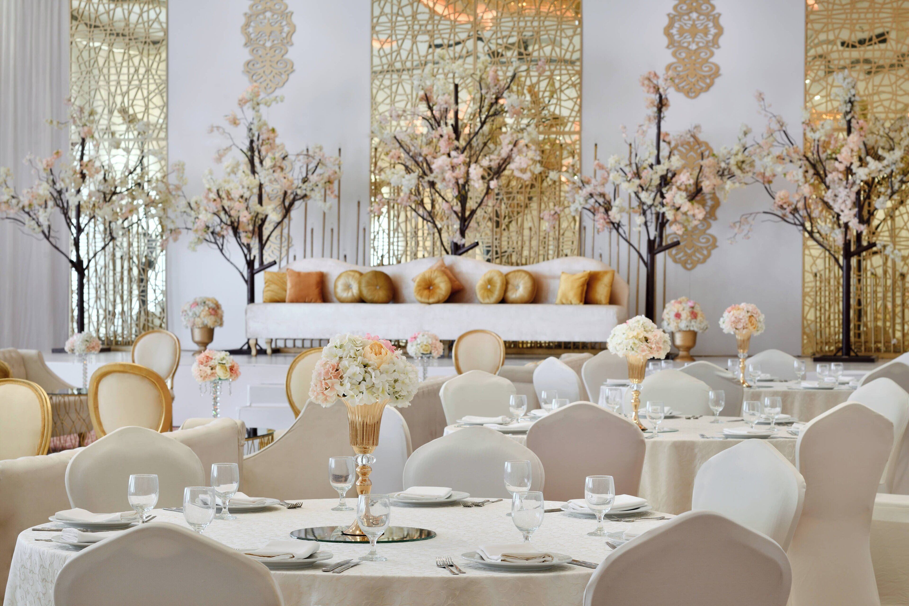 A banquet hall with round tables, white tablecloths, and gold accents.