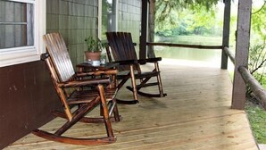 Une terrasse en bois avec deux fauteuils à bascule et une table, donnant sur une étendue d’eau.