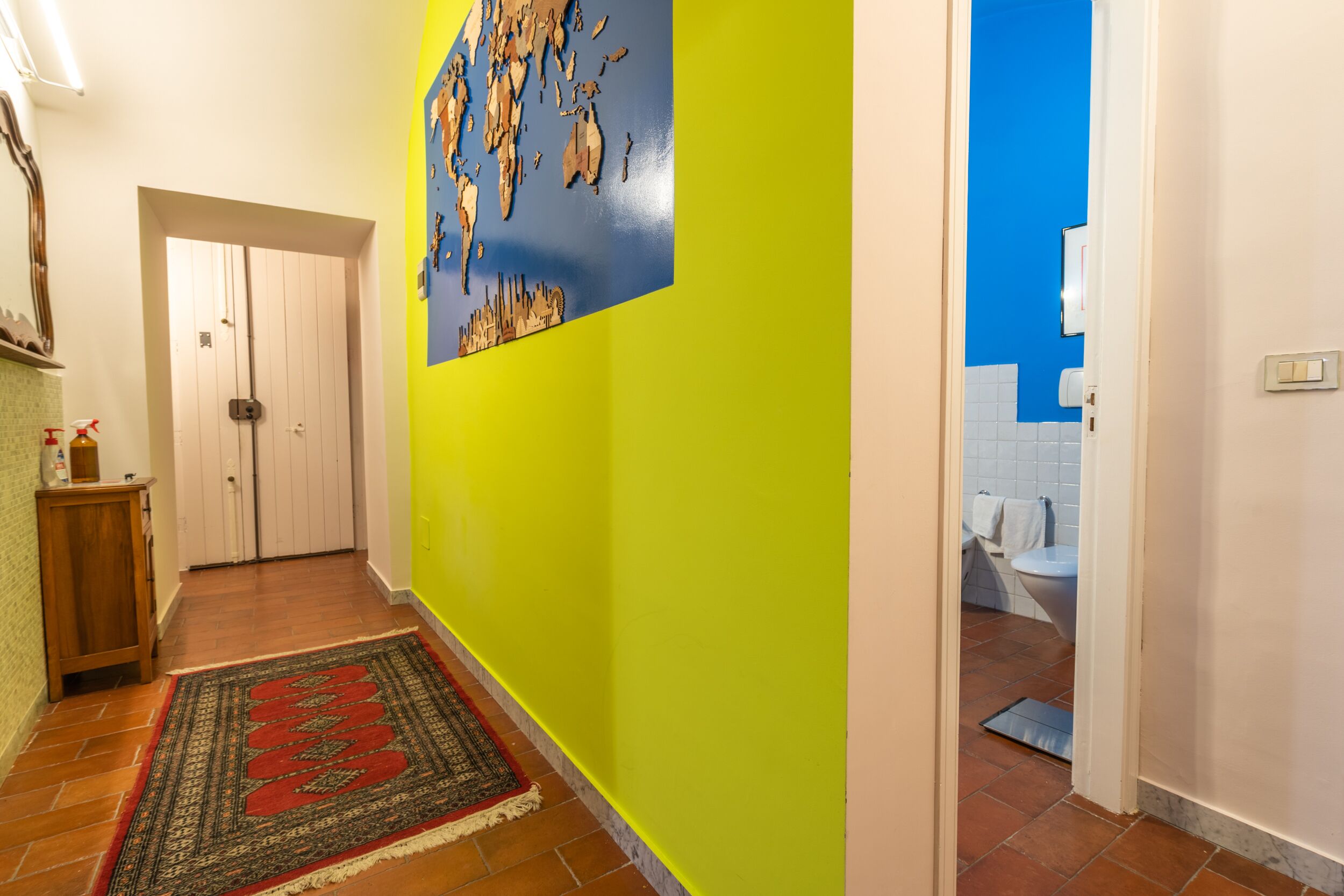 A hallway with a wooden door, a patterned rug, and a wall with a map.