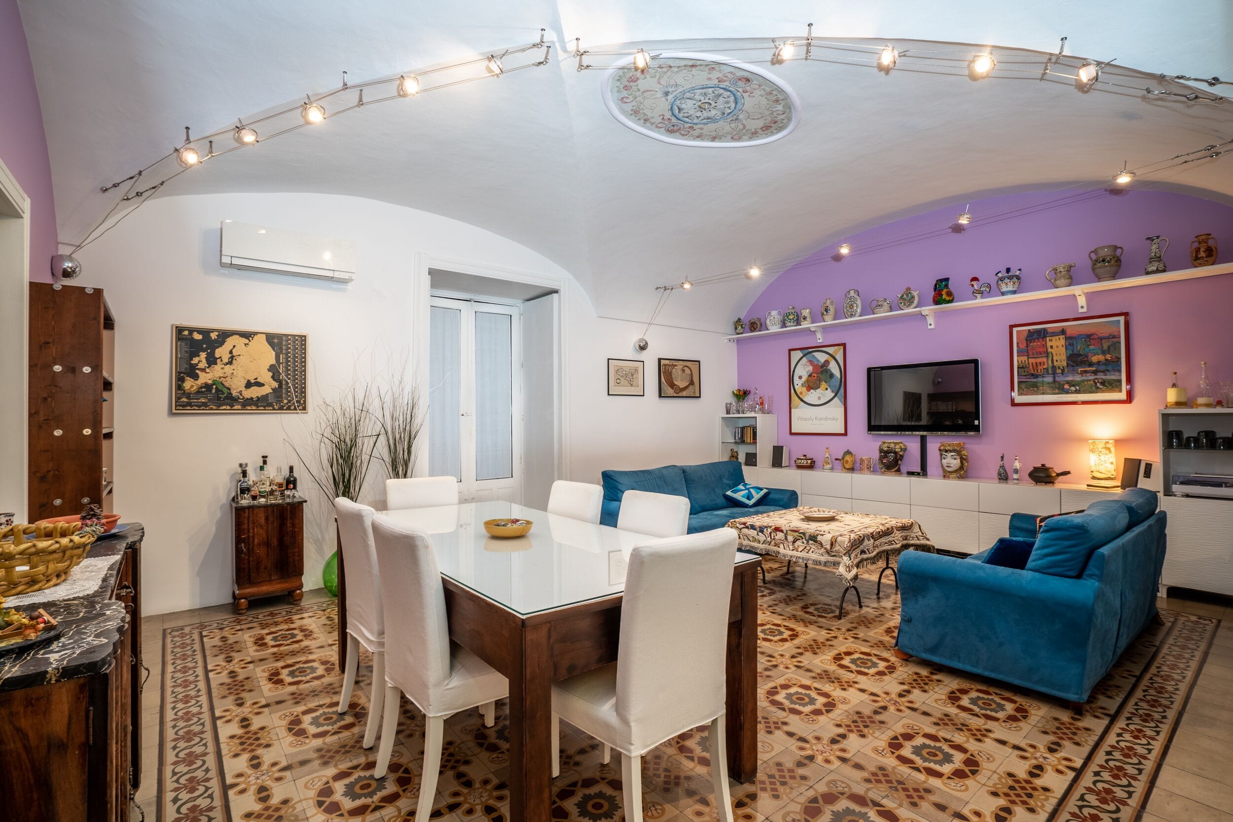 Zona pranzo con tavolo in vetro, sedie bianche e tappeto decorato.