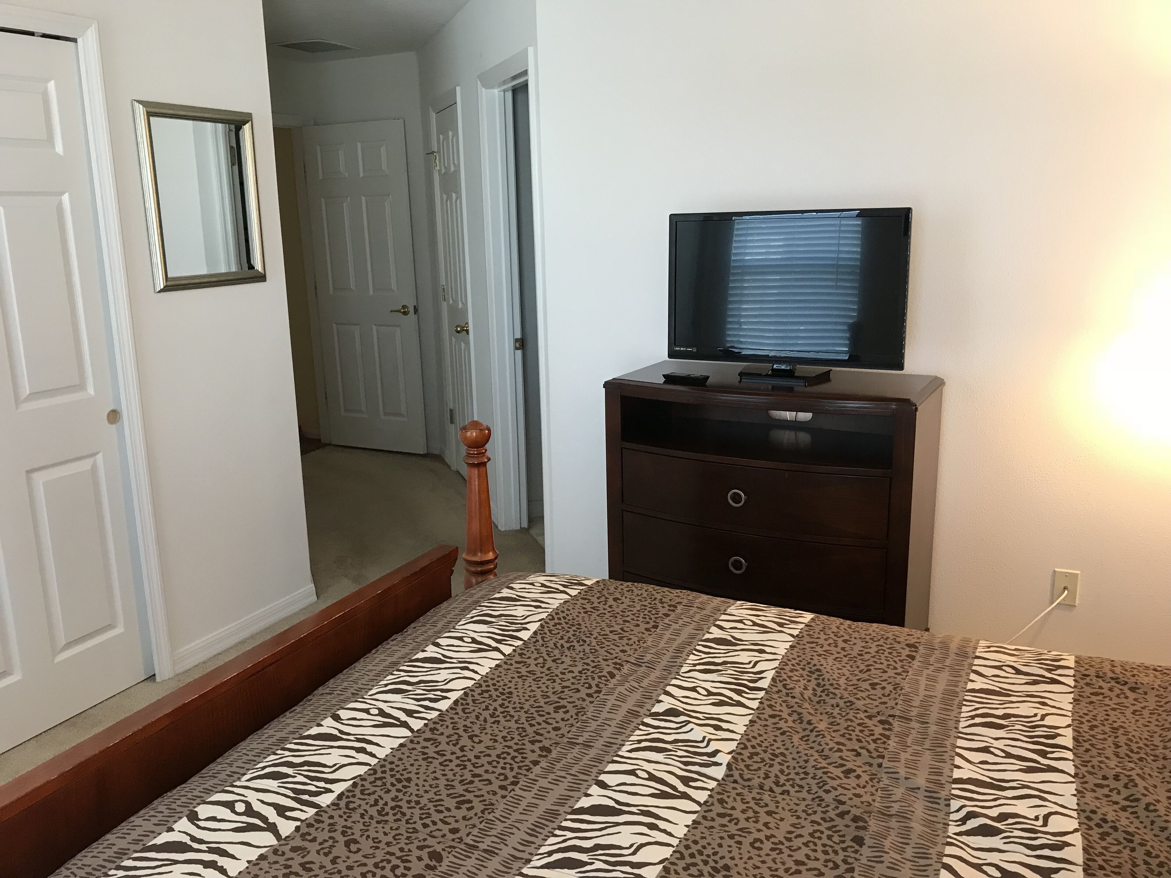 A bedroom with a bed, a dresser, a television, and a door leading to another room.