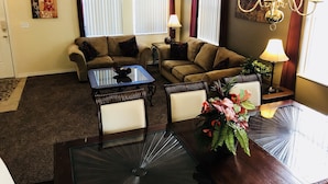 A living room with two sofas, a glass coffee table, a dining table with chairs, a chandelier, and a potted plant. - SOUTH FACING POOL/SPA - ALL DAY SUN - FREE BBQ/WIFI/CALLS - GAMES ROOM - 5 BR (Davenport)