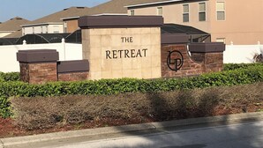 A sign for 'The Retreat' with a logo, surrounded by a hedge and a brick wall. - SOUTH FACING POOL/SPA - ALL DAY SUN - FREE BBQ/WIFI/CALLS - GAMES ROOM - 5 BR (Davenport)